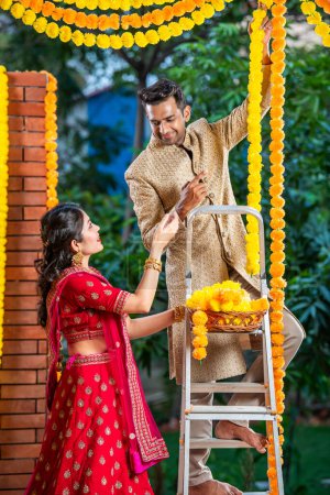 Couple indien décorant porte d'entrée avec guirlandes de fleurs sur diwali ou festival hindou