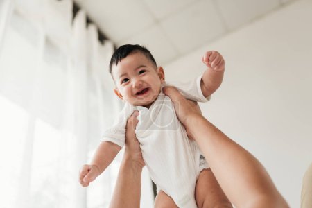 Téléchargez les photos : Asiatique adorable bébé de bonne humeur, Profitez de jouer avec les parents. Un parent tenant un petit bébé et se levant jouant. - en image libre de droit