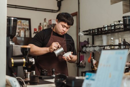 Foto de Barista verter espuma de leche para hacer café arte latte. Un barista asiático que trabaja en una cafetería. Menú de arte latte café, café expreso, concepto de menú de café. - Imagen libre de derechos