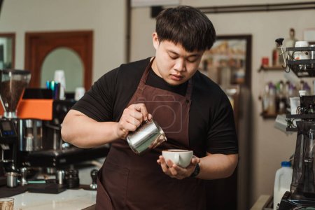 Foto de Barista verter espuma de leche para hacer café arte latte. Un barista asiático que trabaja en una cafetería. Menú de arte latte café, café expreso, concepto de menú de café. - Imagen libre de derechos