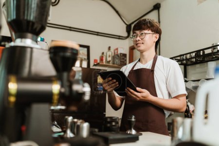 Asian man barista use digital tablet take orders service at coffee shop. SME business coffee shop concept.