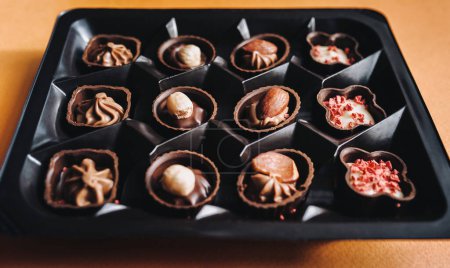 Foto de Hermosos chocolates con nueces están en una caja marrón. De cerca. Fondo naranja. - Imagen libre de derechos