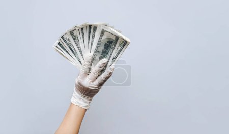 Photo for A man holds money in white medical gloves. Isolated. Gray paper background. The concept of treatment fees, bribes, illegal surgery. Copy space. - Royalty Free Image