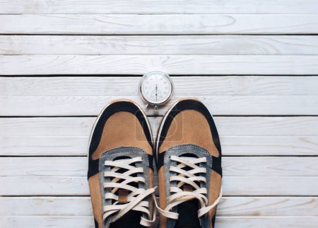 Téléchargez les photos : Belles chaussures de sport beige (baskets) en daim avec chronomètre sur fond blanc rustique en bois. Concept d'entraînement, jogging et sport. Vue du dessus. - en image libre de droit
