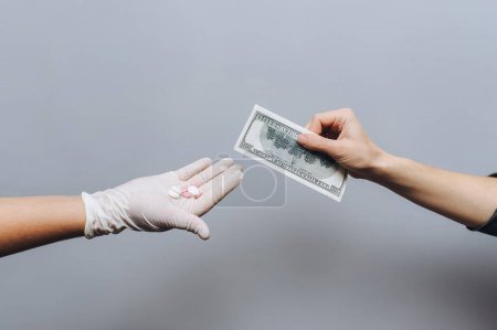 Photo for The doctor's hand in a white medical glove holds pills, and the patient's hand holds out money towards him fee for medicine.Coronavirus vaccine concept.Drug treatment, placebo homeopathy, drug trade - Royalty Free Image