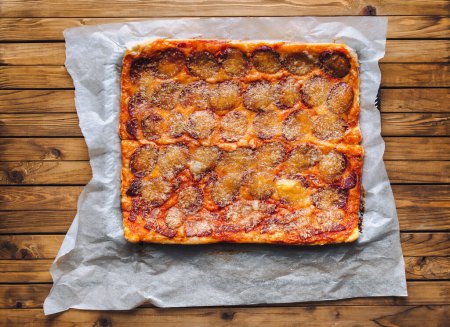 Foto de Pizza casera con queso y salami se encuentra sobre el papiro en el fondo de una mesa de madera marrón. Vista desde arriba. - Imagen libre de derechos