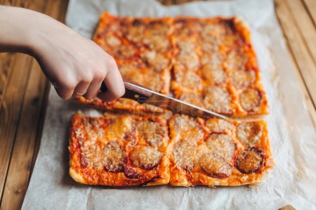 Foto de Pizza cuadrada hecha a mano con salchicha ahumada y queso. Papiro blanco, fondo de madera, primer plano. - Imagen libre de derechos