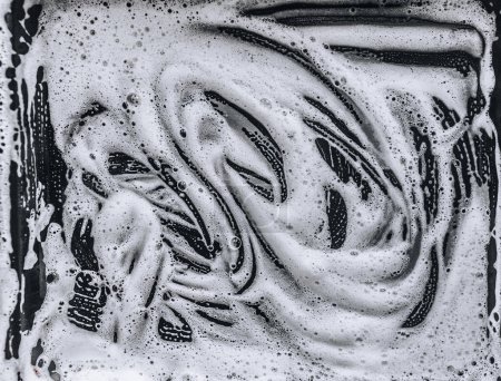 Foto de Espuma blanca y jabón sobre fondo oscuro. Patrón abstracto. El concepto de lavado de la cacerola aceitosa o coche negro. - Imagen libre de derechos