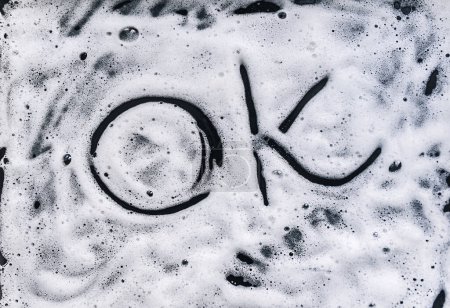 Foto de La palabra "Ok" está escrita en una espuma jabonosa. Detergente para sartén, vajilla o coche. - Imagen libre de derechos