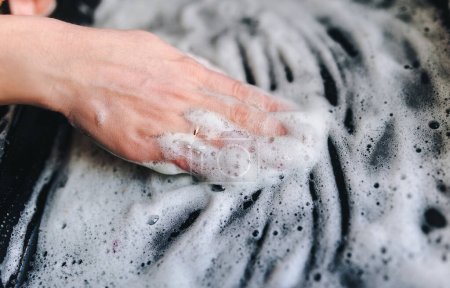 Foto de La ama de casa usa líquidos para lavar. La mano lava la superficie sucia con una solución de jabón. El trabajo de las mujeres en la migración laboral. - Imagen libre de derechos