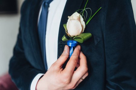 Téléchargez les photos : Le marié met sur sa boutonnière de mariage. Préparation du mariage. Ajuster la veste fleur. - en image libre de droit