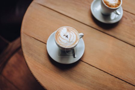Photo for Two cups of morning coffee on a wooden round table. Coffee for a couple. Cappuccino, latte, foam. - Royalty Free Image
