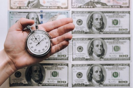 Téléchargez les photos : Main de femme tenant un chronomètre gris sur fond de dollars. Concept de crédit. Temps pour l'argent rapide. - en image libre de droit