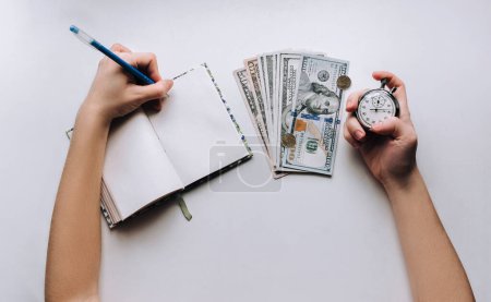 Téléchargez les photos : Dollars, cahier, stylo. Main de femme tenant un chronomètre gris sur fond blanc. Habitué, concept de crédit. Temps pour l'argent rapide. - en image libre de droit