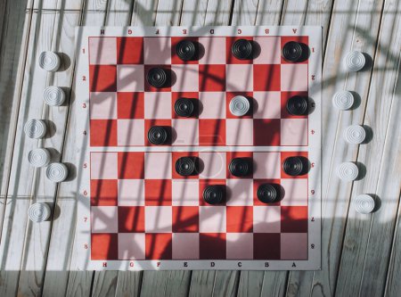 Photo for White and black checkers on a paper chessboard with pink and red cells. View from above. Logik game concept. - Royalty Free Image