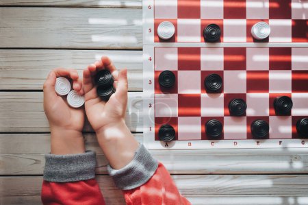 Photo for The child plays checkers. White and black checkers in children's hands. Children's school of board games. - Royalty Free Image