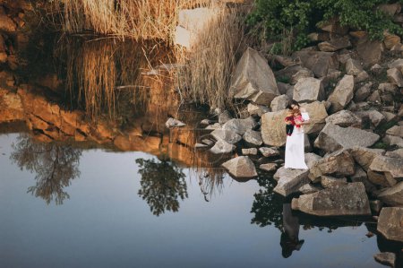 Foto de Joven mujer de aspecto modelo de pie sobre las piedras cerca del río con dos muñecas en las manos. Una adolescente se imagina que es madre. - Imagen libre de derechos