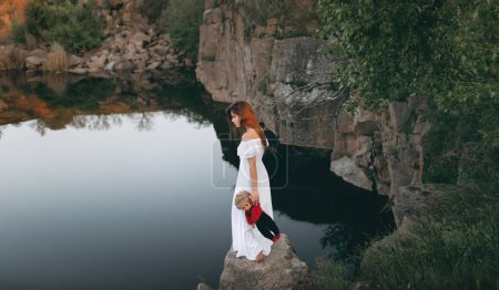 Foto de Joven mujer de aspecto modelo de pie sobre las piedras cerca del río con dos muñecas en las manos. Una adolescente se imagina que es madre. - Imagen libre de derechos