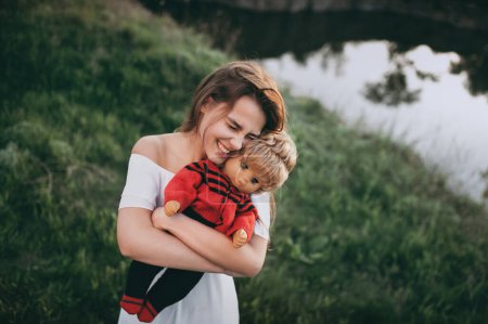 Téléchargez les photos : Jeune femme mannequin avec un visage heureux étreint sa poupée préférée. Une adolescente joue avec sa poupée dès l'enfance. - en image libre de droit