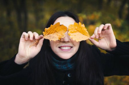 Téléchargez les photos : Belle jeune femme les yeux fermés avec des feuilles d'automne. Fille souriant à la caméra. En plein air. Des vacances. Automne. - en image libre de droit
