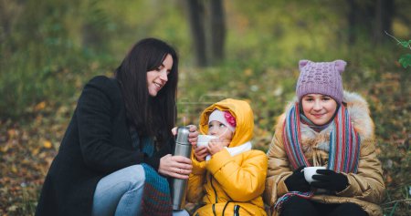 Foto de Los niños beben té caliente de un termo durante un paseo por el bosque de otoño. Caminatas familiares. - Imagen libre de derechos