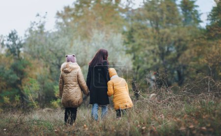 Téléchargez les photos : Vue arrière de la randonnée en famille à travers la forêt en automne. - en image libre de droit