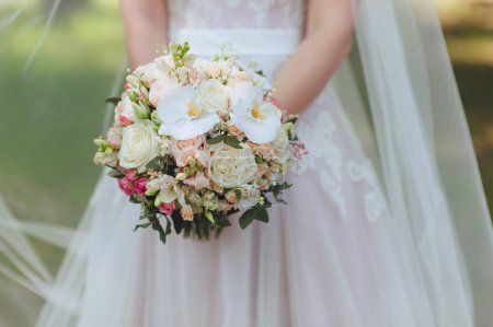 Foto de La novia en un vestido blanco está sosteniendo un hermoso ramo de bodas en sus manos. Orquídeas blancas y rosas. Flores delicadas. - Imagen libre de derechos
