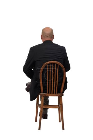 Foto de Vista trasera de un hombre calvo sentado en una silla con patas cruzadas sobre fondo blanco - Imagen libre de derechos