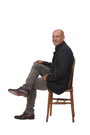Foto de Vista lateral de un hombre sentado en una silla con las piernas cruzadas mirando a la cámara sobre fondo blanco - Imagen libre de derechos