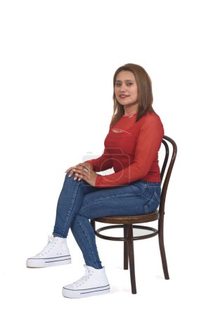 Foto de Vista lateral de una mujer sentada en una silla con piernas cruzadas y mirando a la cámara sobre fondo blanco - Imagen libre de derechos