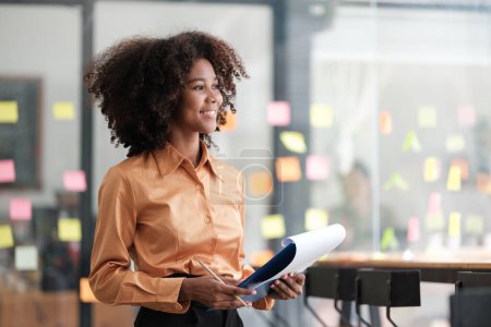 Photo for Close up of focused african American female employee write down on colorful sticky notes manage list, concentrated biracial woman work on startup brainstorm collaborate plan on stickers on glass wall - Royalty Free Image