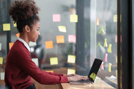 Photo for Close up of focused african American female employee write down on colorful sticky notes manage list, concentrated biracial woman work on startup brainstorm collaborate plan on stickers on glass wall - Royalty Free Image