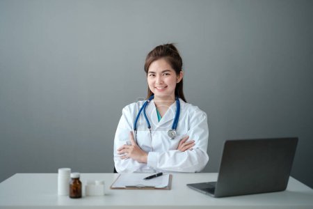 Porträt einer glücklichen schönen asiatischen Ärztin, die ihre eigene Praxis hat. Lächelnde europäische Ärztin oder Kardiologin in weißer Laborkittel-Uniform sitzt am Schreibtisch in ihrem modernen Büro. Hochwertiges Foto