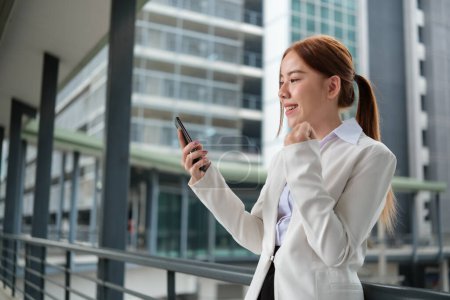 Asiatische Unternehmerin feiert Erfolg mit Erfolg. Frau mit Smartphone bei der Arbeit außerhalb des Büros mit erhobener Hand und glücklicher Triumphgeste. Hochwertiges Foto