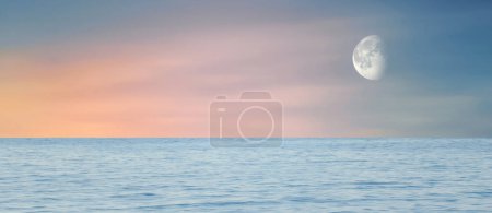 Wide sea view at sunset. Orange sun rays and moon in cloudless sky. Amazing landscape.