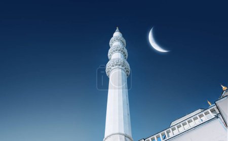 Bottom-up view of mosque minaret. Islamic background photo. Shining crescent in the sky. Background image for islamic holidays and greeting card.