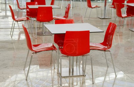Empty red chairs and white table in food court in shopping mall. No customers, empty tables and chairs.