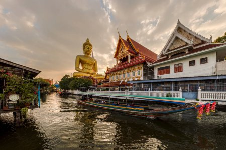Foto de Un barco estaba pasando la estatua de Buda Grande (Phra Buddha Dhammakaya Thepmongkhon) en el templo de Wat Pak Nam Phasi Charoen situado junto al río durante la puesta del sol. - Imagen libre de derechos