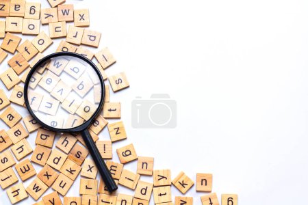 Photo for English alphabet made of square wooden tiles with the English alphabet scattered on white background. The concept of thinking development, grammar. Magnifier placed on English letters - Royalty Free Image
