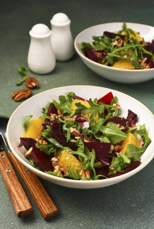 Salad with arugula, orange and beet in a plate on a green background