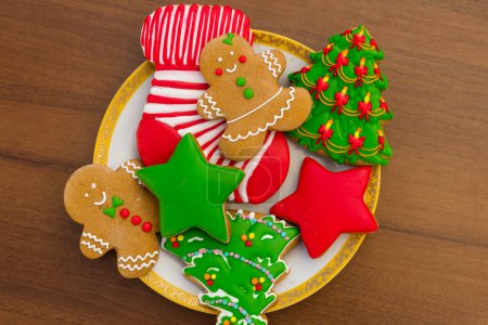 Photo for Plate with tasty festive Christmas cookies in the shape of Christmas tree, Gingerbread man, star and Christmas sock on wooden table. Top view - Royalty Free Image