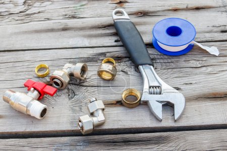 Photo for Various plumbing spare parts, sealing tape and adjustable wrench on rustic wooden background - Royalty Free Image
