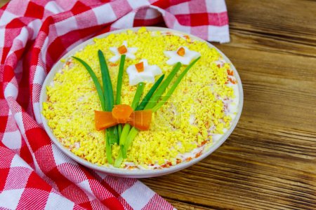 Traditional russian layered salad Mimosa with spring decoration Daffodil on wooden table. Decoration is made of egg, green onion and carrot