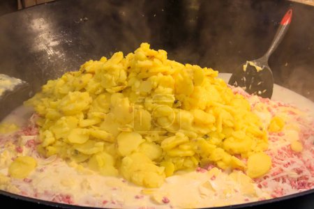 Zubereitung von Tartiflette, einem traditionellen französischen Gericht aus Kartoffeln, Speck und Käse, in einem großen Kessel