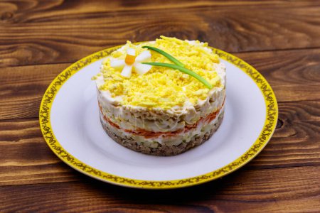 Traditioneller russischer Schichtsalat Mimosa mit Frühlingsdekoration Narzissen. Dekoration besteht aus Ei, grüner Zwiebel und Karotte