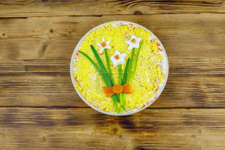 Traditional russian layered salad Mimosa with spring decoration Daffodil on wooden table. Top view. Decoration is made of egg, green onion and carrot
