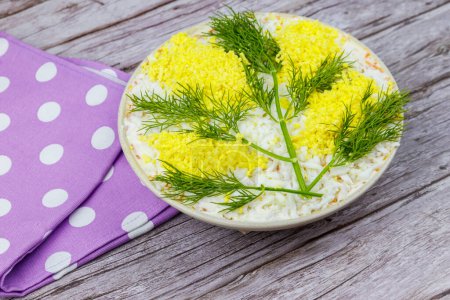 Traditional russian layered salad Mimosa decorated with sprigs of mimosa (made of eggs yolk and dill) on wooden table
