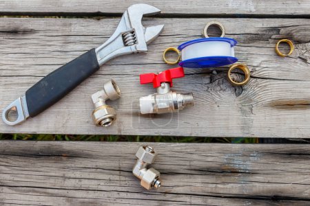 Photo for Various plumbing spare parts, sealing tape and adjustable wrench on rustic wooden background. Top view - Royalty Free Image