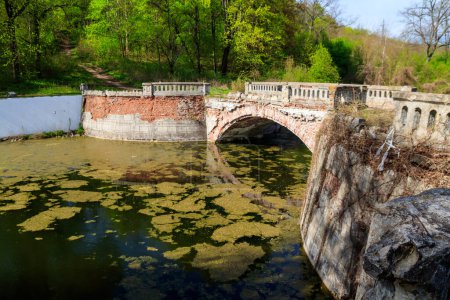 Alte gebogene Ziegelbrücke über einen Teich im Sharovka Palace Park im Gebiet Charkow, Ukraine