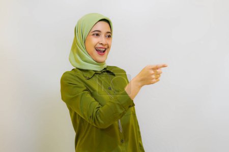 Foto de Joven chica asiática con traje verde señalando algo alegremente. Concepto publicitario - Imagen libre de derechos